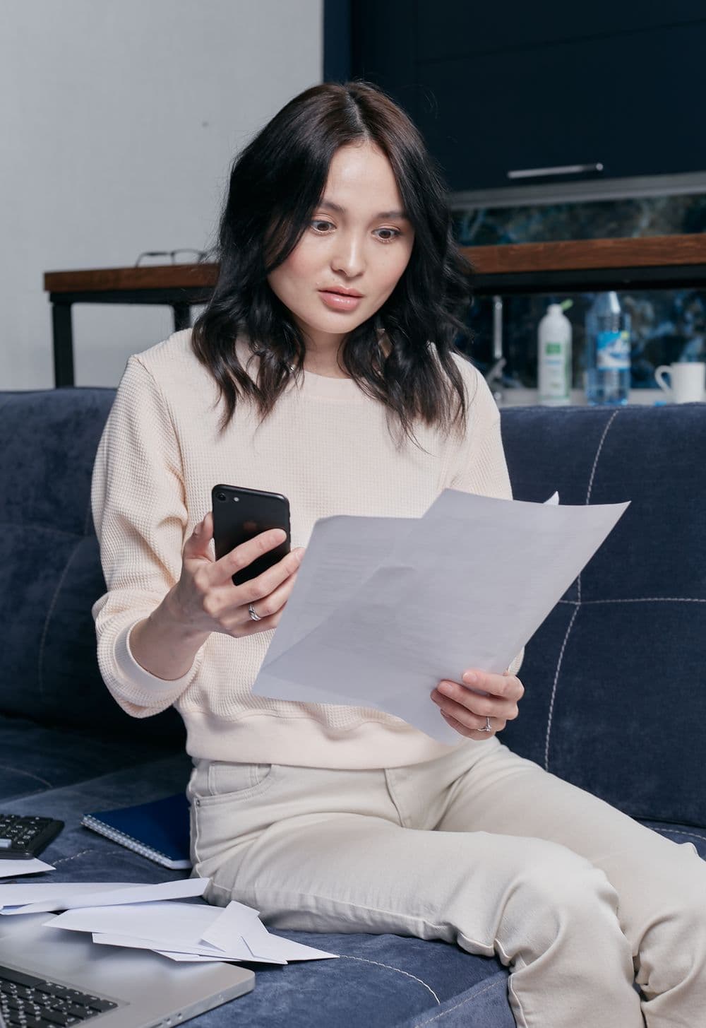 A business owner on her couch with a stack of papers in one hand and her phone in the other.