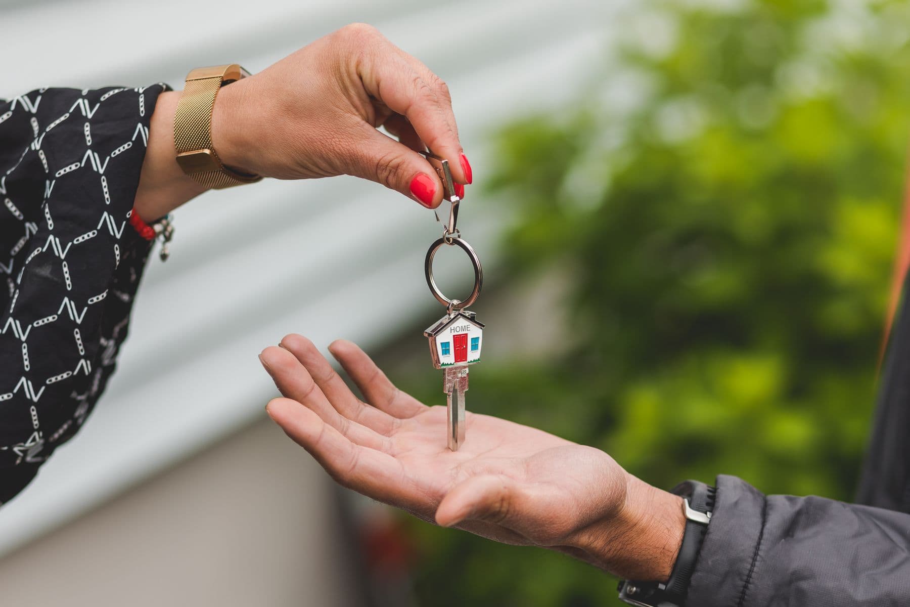 One hand passing a house key on a house-shaped key ring into another open hand.