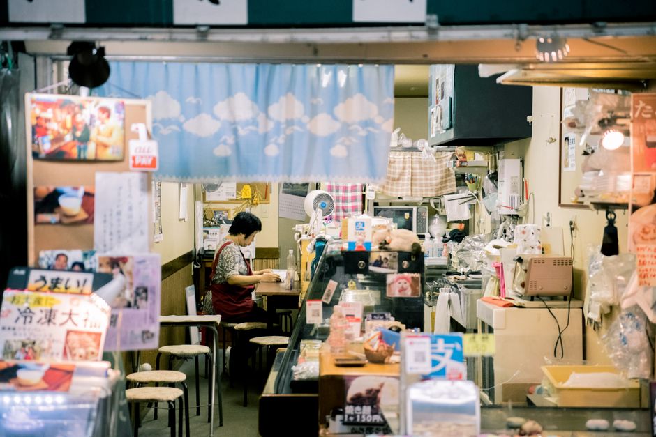 Warm interior of a cozy small shop in Osaka, featuring an Asian woman working, surrounded by local goods and decor.